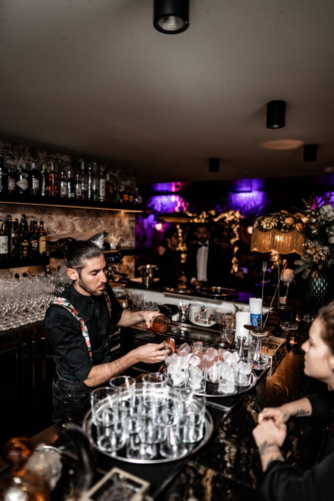 A bartender at a busy wedding bar pours drinks for a wedding guest with many other people standing around. Tips for setting up your bar service. 