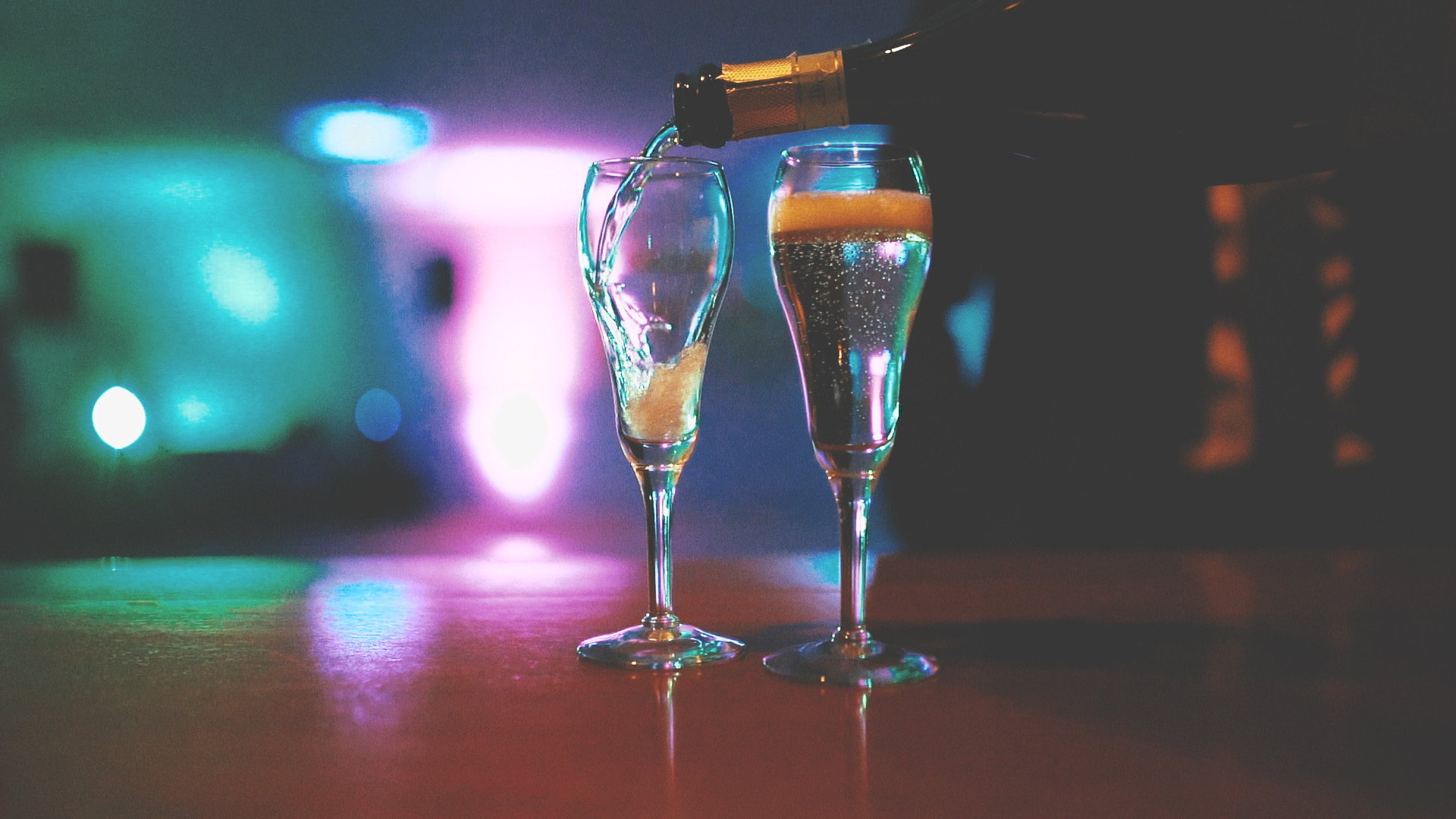 Two champagne glasses being filled with up-lit background