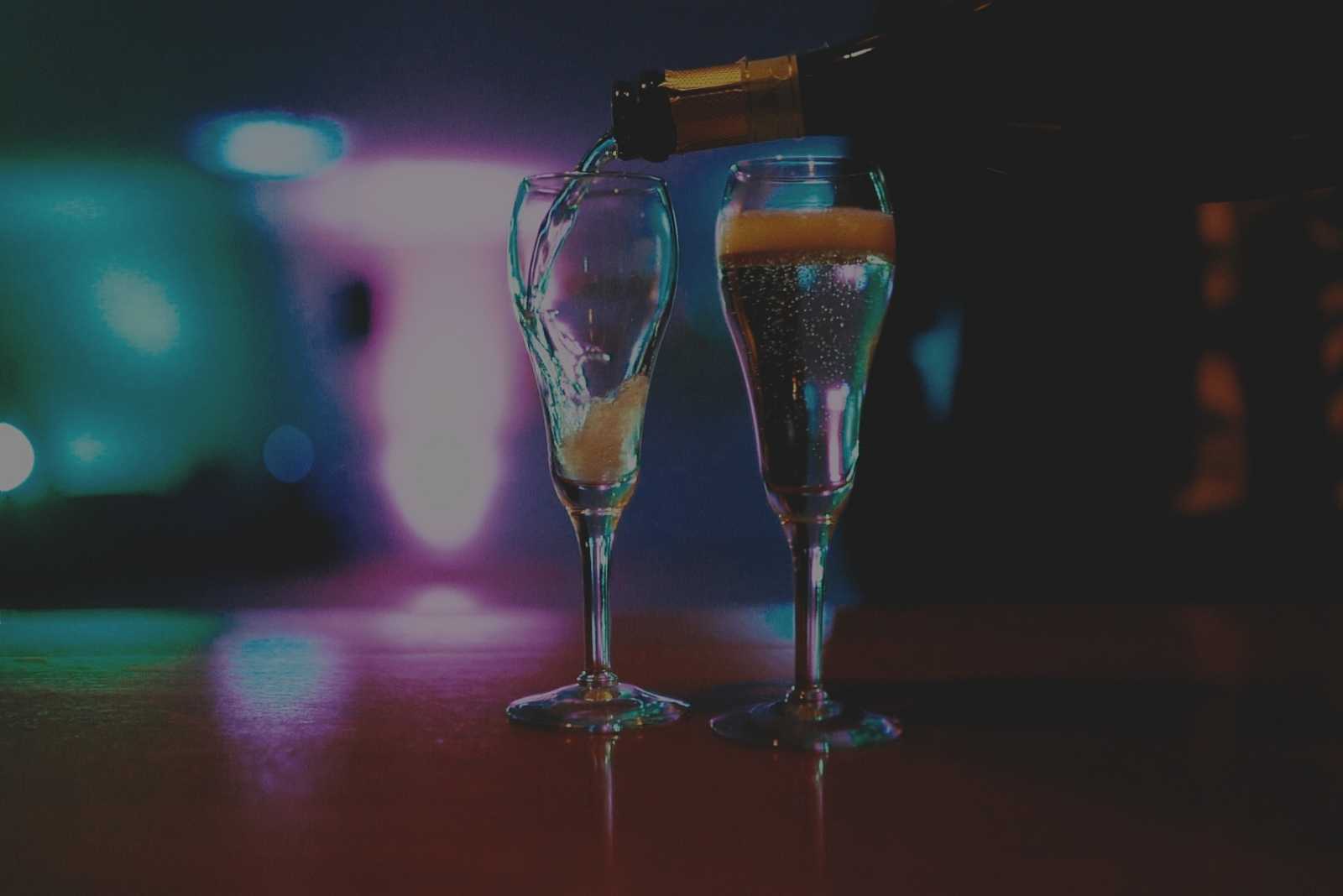 Two champagne glasses being filled with up-lit background