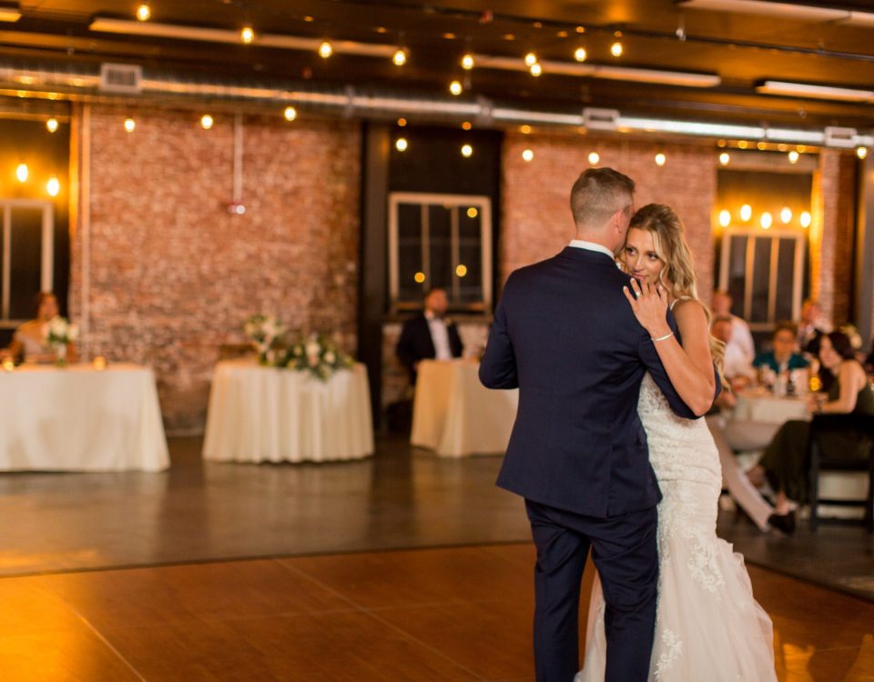 Bride and groom sharing their first dance under bistro lights with a brick backdrop at The Venues Toledo special event venue