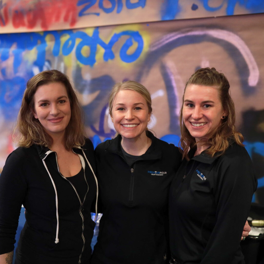 Premier Pour Bartending team members Amanda, Abby, and Liv at the St. John's Jesuit event "Dinner Under the Dome" in front of a graffiti style backdrop