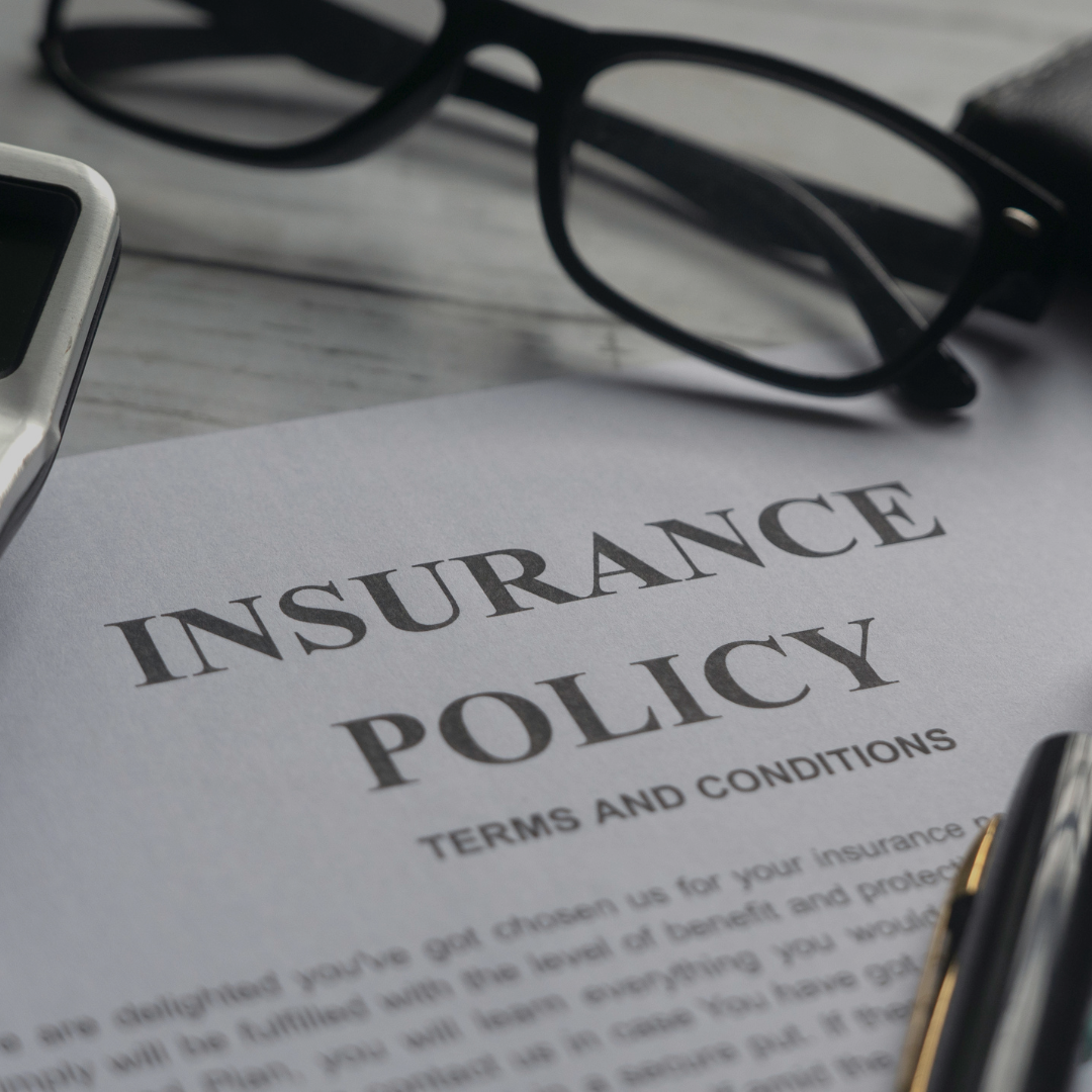 White piece of paper with the words Insurance Policy and a pair of glasses sitting at the top of the page.