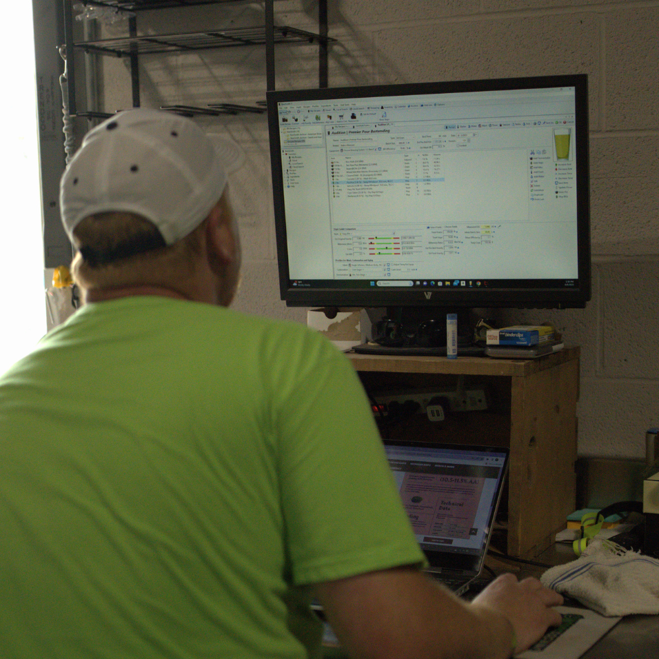 Oncore Brewing owner, Keith Baker, in a safety green t-shirt working on the computer to create the recipe for the beer Audition